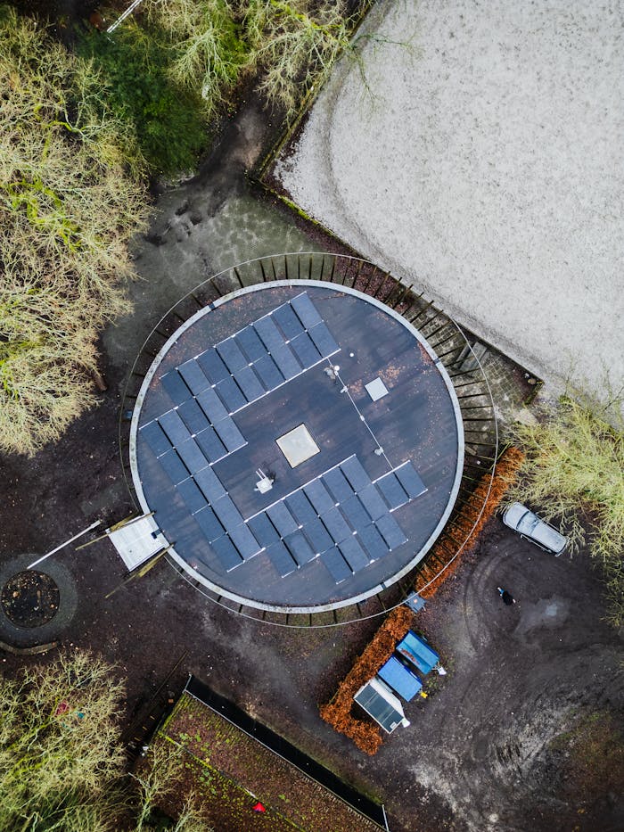 Drone shot of a circular rooftop covered with solar panels surrounded by trees.